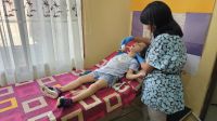 Tamara lies on a clinic bed. Beside her stands Laura Giovana, holding a facial massager in her hand, which she passes gently over the little girl's cheek.