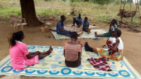 A group of people sit on blankets under a tree during a community mental health awareness session.