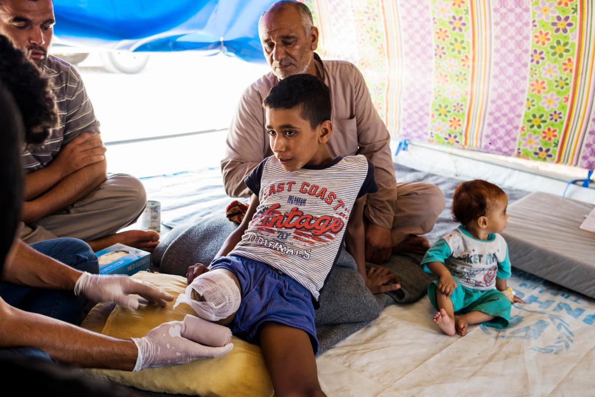 Mohammad changes the dressing on Abdel Rahman's wound while his father Ahmed looks on. 
