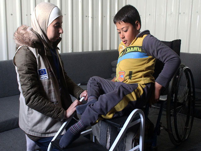 Noor helps Ahmad to get used to his wheelchair. Jordan.