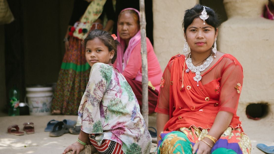 An elderly woman, young woman, and young girl sit outside their home in Nepal.