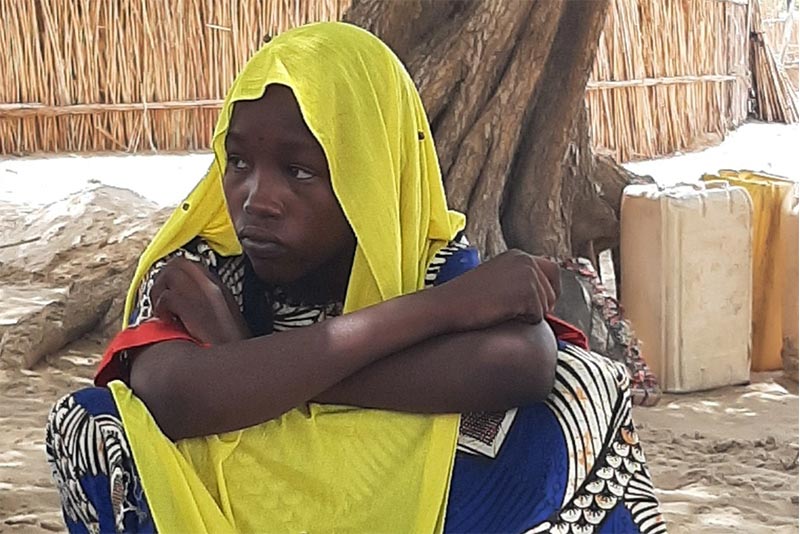 Hawa sitting on the floor with her arms crossed and her back to a tree.