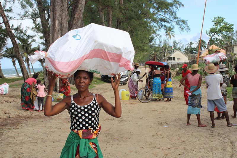 A woman carries a household kit on her head, including cooking utensils, blankets, candles and more.