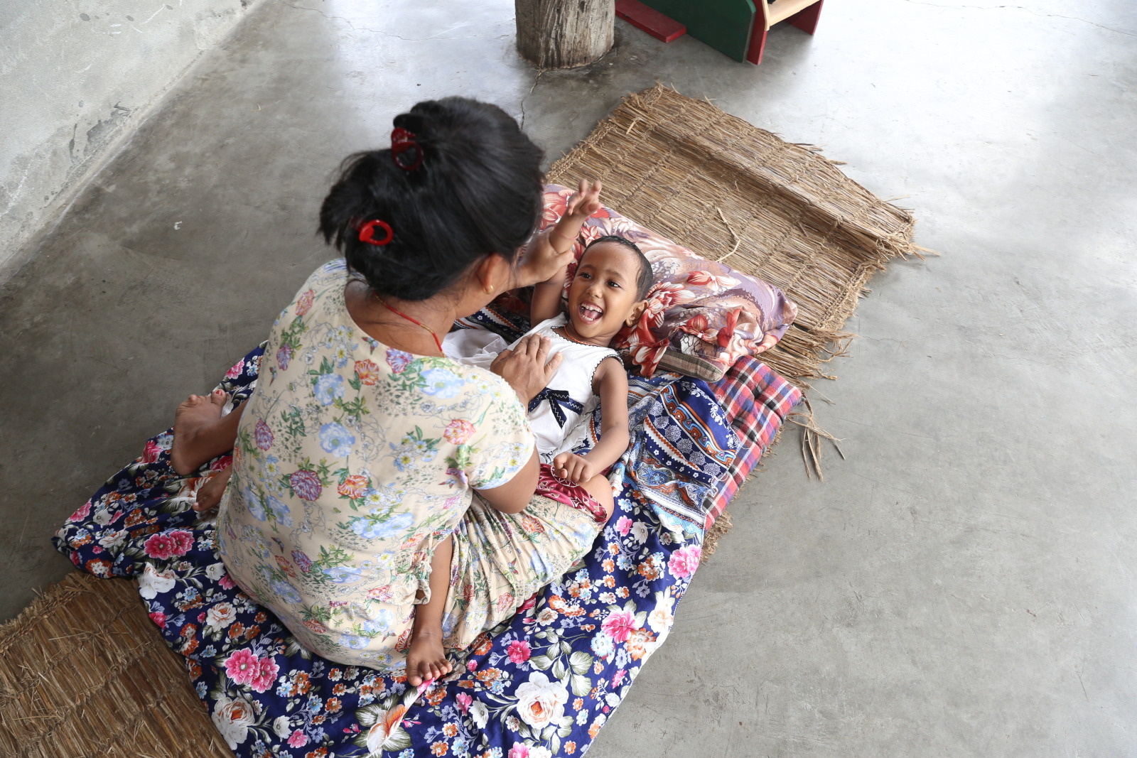 A young girl lies on a blanket while her mother helps raise her arm above her head.
