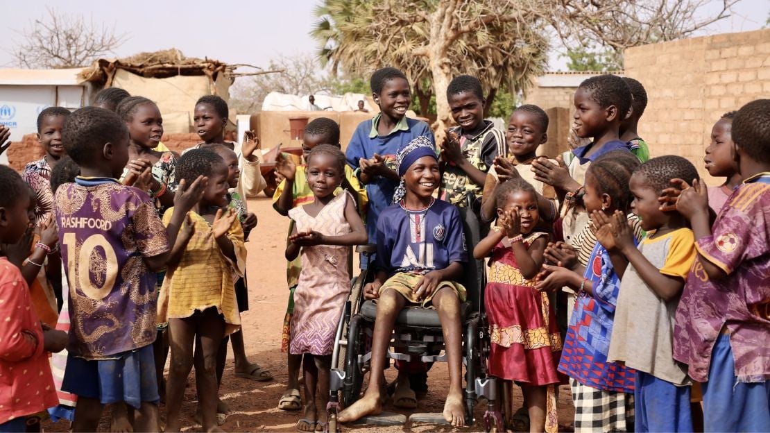 A group of children. A girl in the middle sits in a wheelchair.