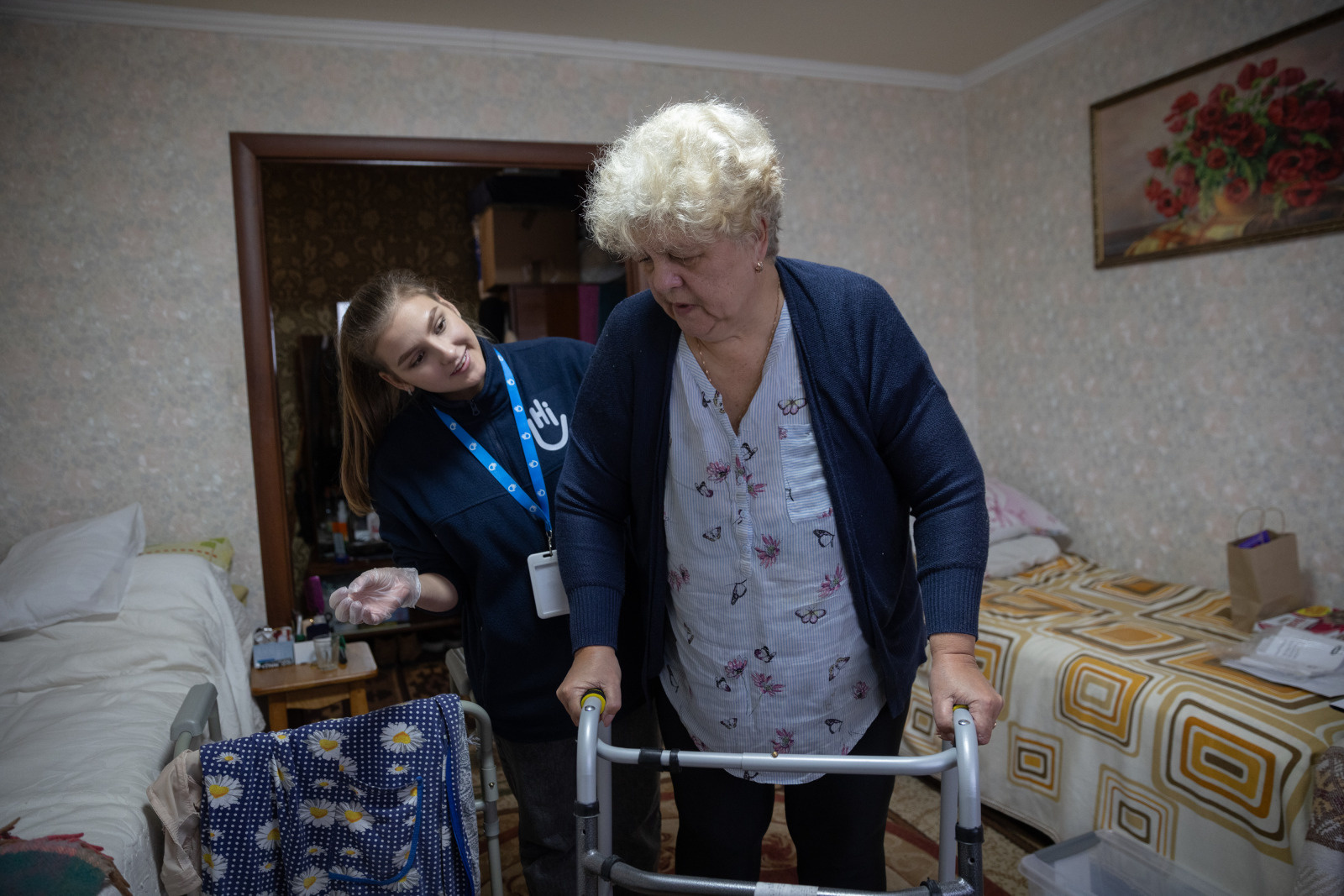 A older woman stands with a walker. An HI physical therapist stands behind her.