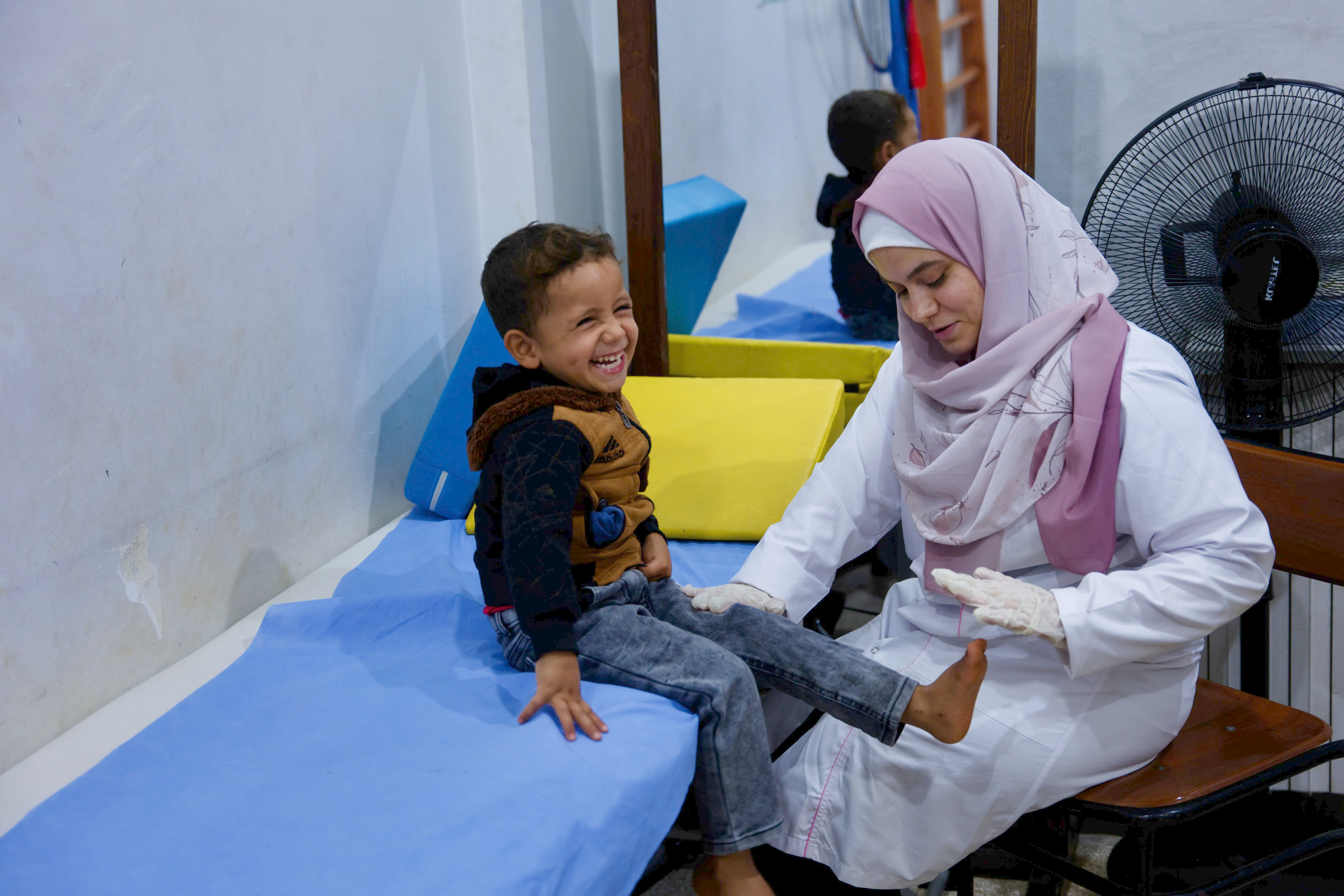 A young boy smiles as a physical therapist helps him with exercises