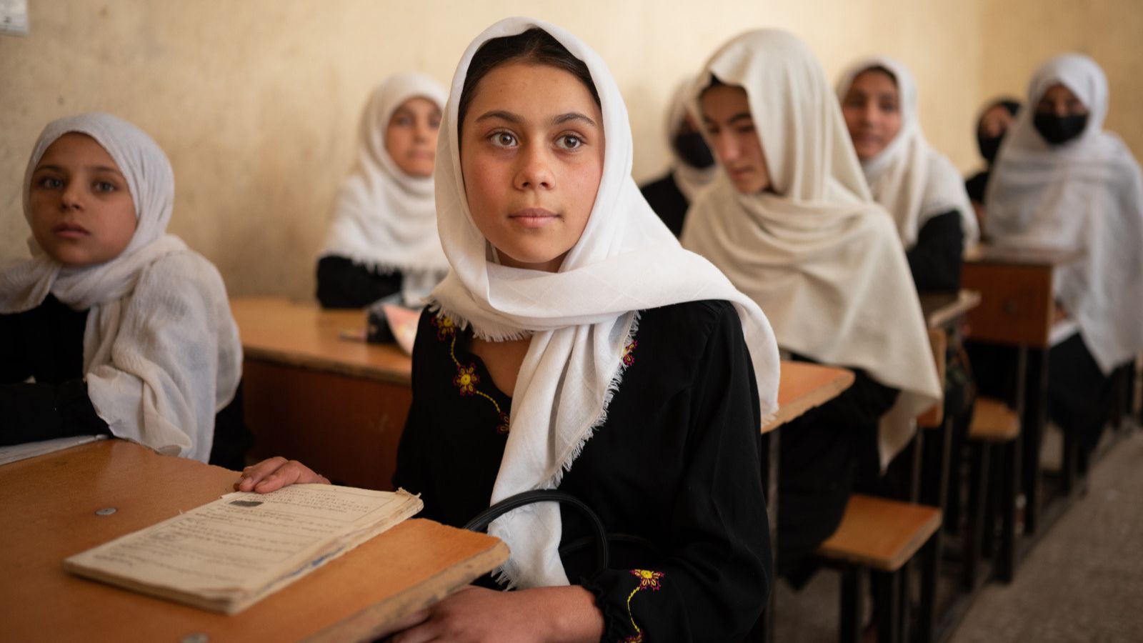 Afghan girls wearing white head scarves sit at school desks