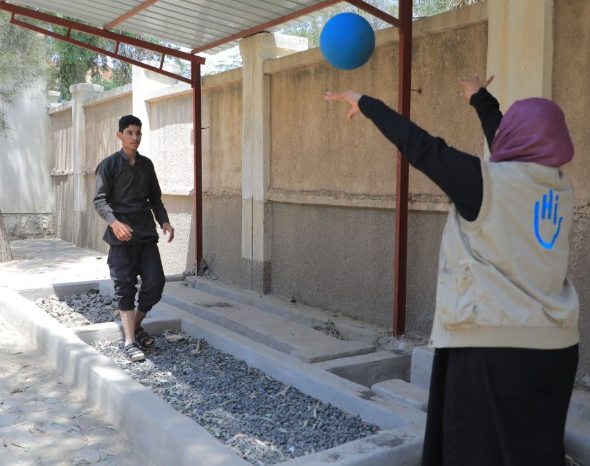 A teenage Yemeni boy wearing an artificial limb catches a ball thrown by an HI rehabilitation specialist