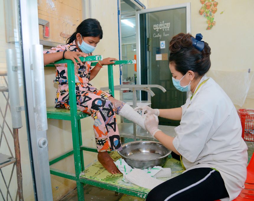 A Cambodian girl sits on a chair while a technician fits her for an artificial limb