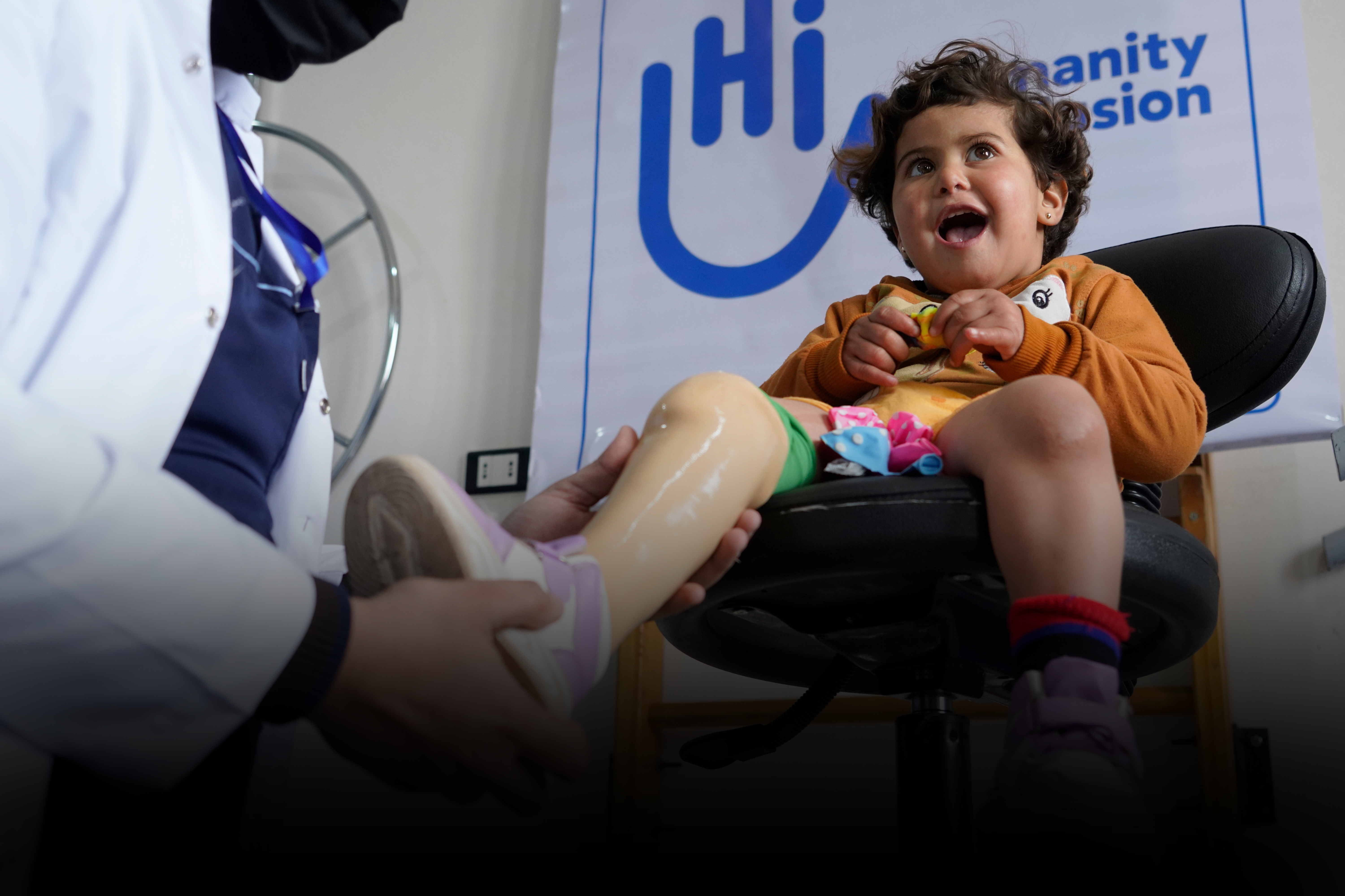 A young girl smiles as a doctor adjusts her prosthetic leg