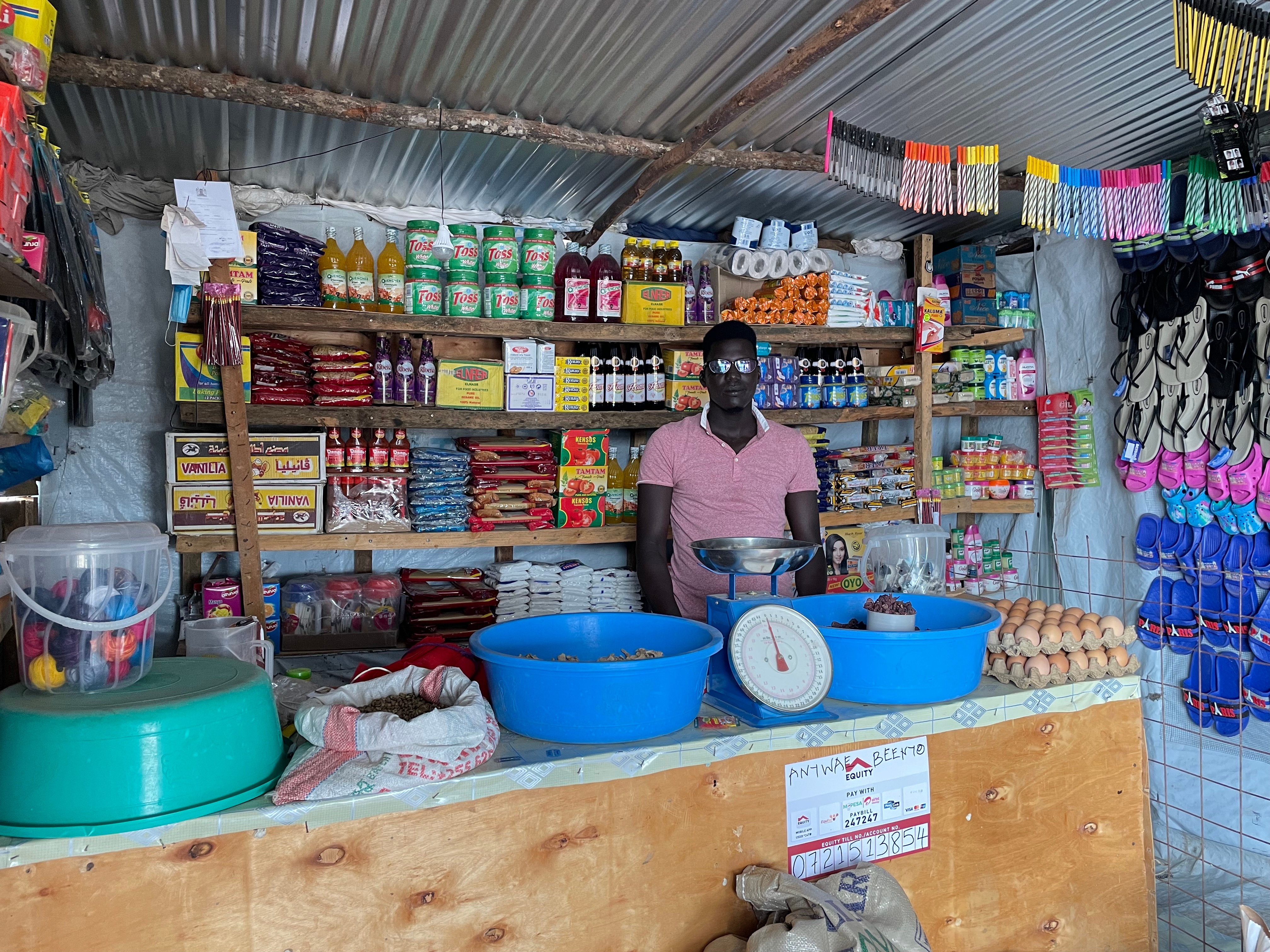 A Black man with glasses stands in a fully stocked shop