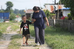 Ambika, looking down, holding hands, and walking with Prabin, 6, who just received a new prosthesis.