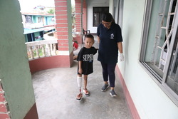 Young boy trying out his new leg prosthetic, being led by a P&O specialist in an outdoor balcony hallway