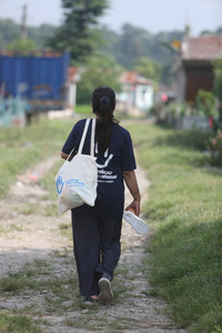 Young woman turned back towards the camera, walking on a track with an HI bag and t-shirt, in Nepal