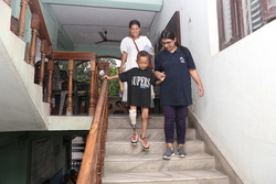 Young boy being led down stairs by P&O specialist as he tries out his new prosthetic leg
