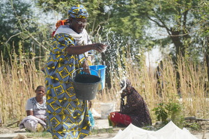 A woman holding a bucket is watering her garden in Léré. © MAEFILMS / HI