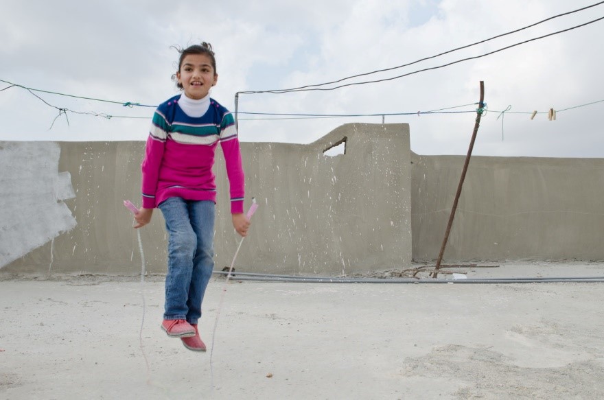 Young girl smiling, skipping rope on a concrete area