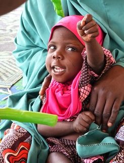 Massalouka, a young girl wearing a pink head covering, tries to grab her toy during a stimulation therapy session. © J. Labeur / HI