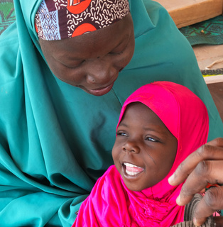 Massalouka, a young girl wearing pink head covering, and her mother, Manssoura wearing a teal head covering, both smile. © J. Labeur / HI