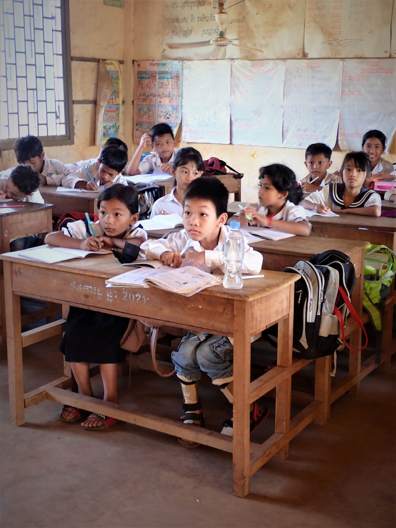 Kham Chanreaksa can attend class thanks to the orthoses supplied by HI. He is in the front row writing in his notebook. 