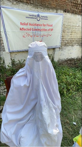 Woman wearing facial and body covering in front of a relief assistance banner