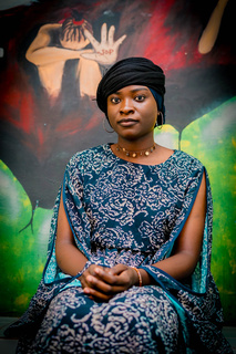 Awa posing in front of a mural painted to raise awareness to sexual violence . © A. Faye / HI