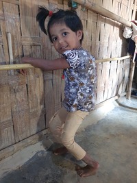 A little girl smiles as she supports herself on a bamboo bar because she can't stand on her own.