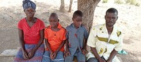 Family of four (twins, mother, and father) seated on a bench in front of a tree