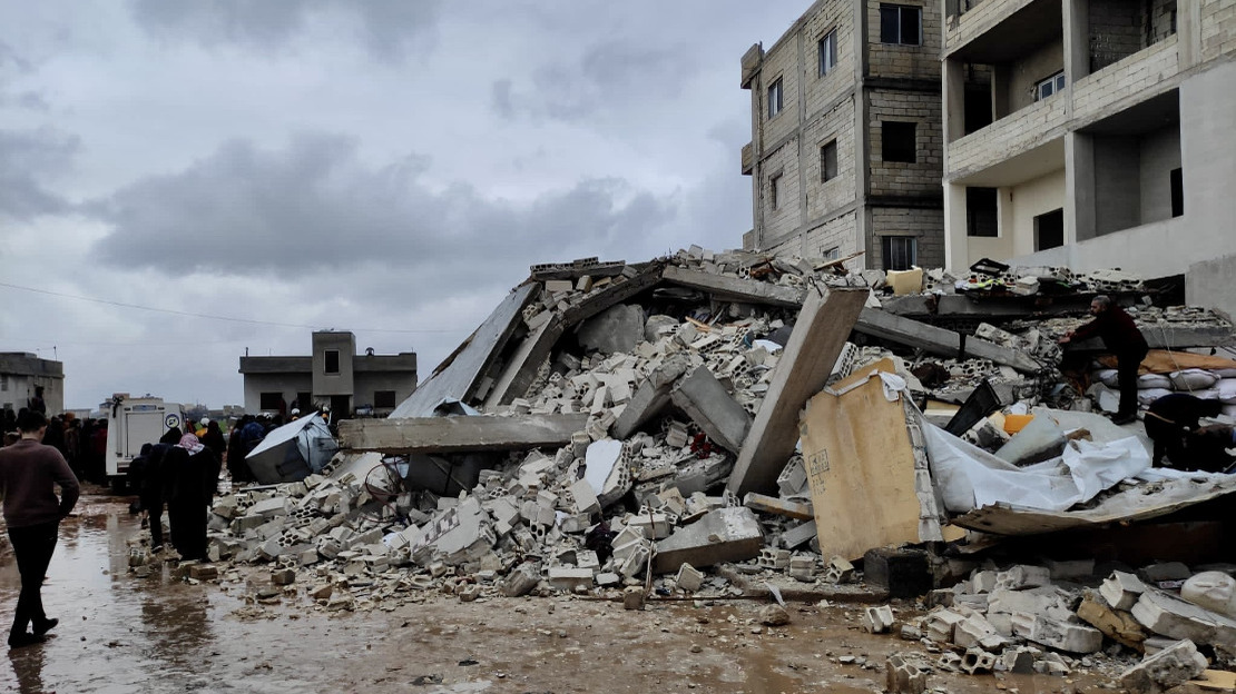 People standing to the side of a collapsed building