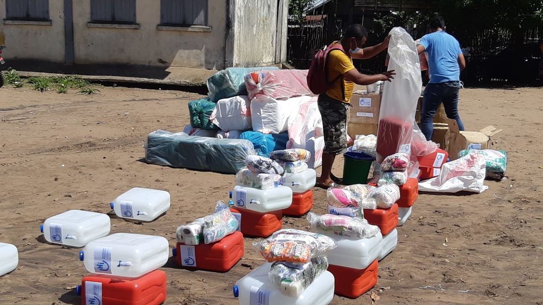 Two men standing amid rows and piles of supply kits, unboxing and unwrapping supplies