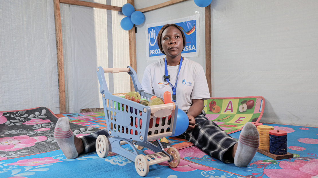 Portrait of Vanessa sitting in a room. She is holding a ball in her hands and around her are children's toys.