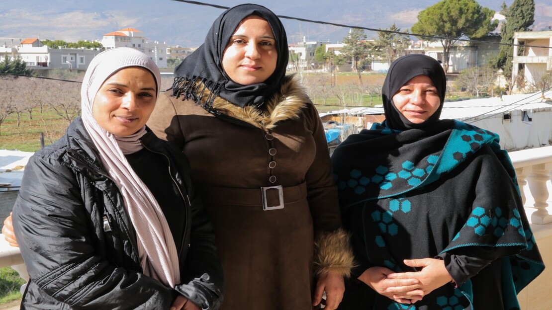 Three women, all wearing head scarfs, standing together side by side. 