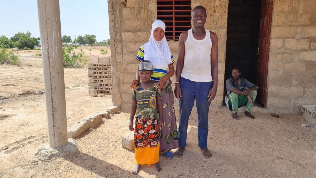 A man, a teenager and a little girl are standing in front of a brick house and smiling.
