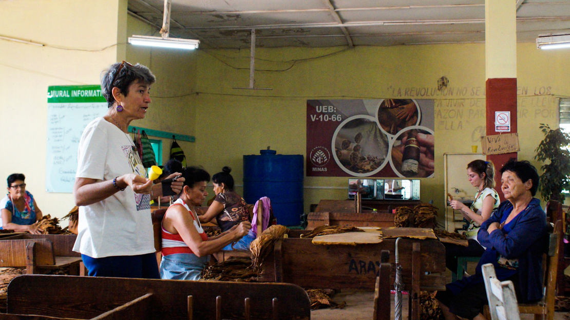 In one room, a woman holds a menstrual cup and explains how it works. Other women sit on benches around her and listen.