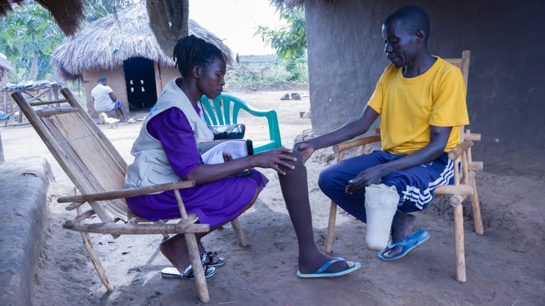 An HI worker and a man are sitting down, discussing the man’s prosthesis.