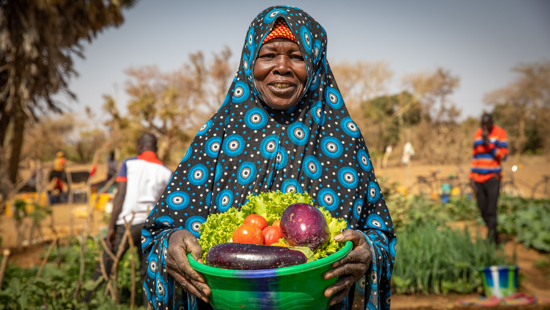 Fadima poses with a bowl of tomatoes, eggplants and lettuce in her hand. The shared garden can be seen in the background.