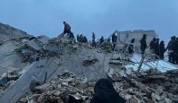 About 20 people standing atop a collapsed building's rubble