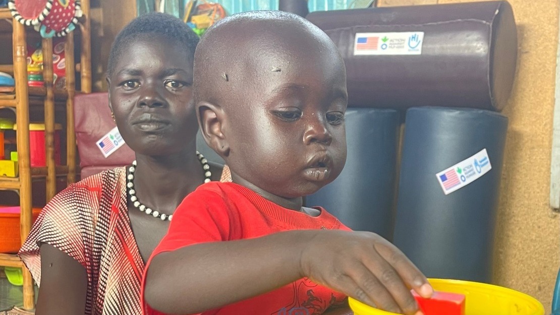 Young girl next her mother in a stimulated therapy session for malnourished children, her hand in a bowl