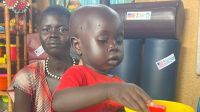 Young girl next her mother in a stimulated therapy session for malnourished children, her hand in a bowl