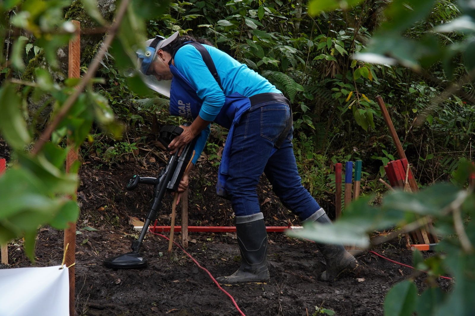 A deminer wearing a uniform and protective gear at work on a plot of land