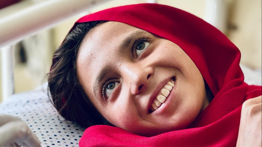 Close-up portrait of a young girl lying on a bed with a big smile.