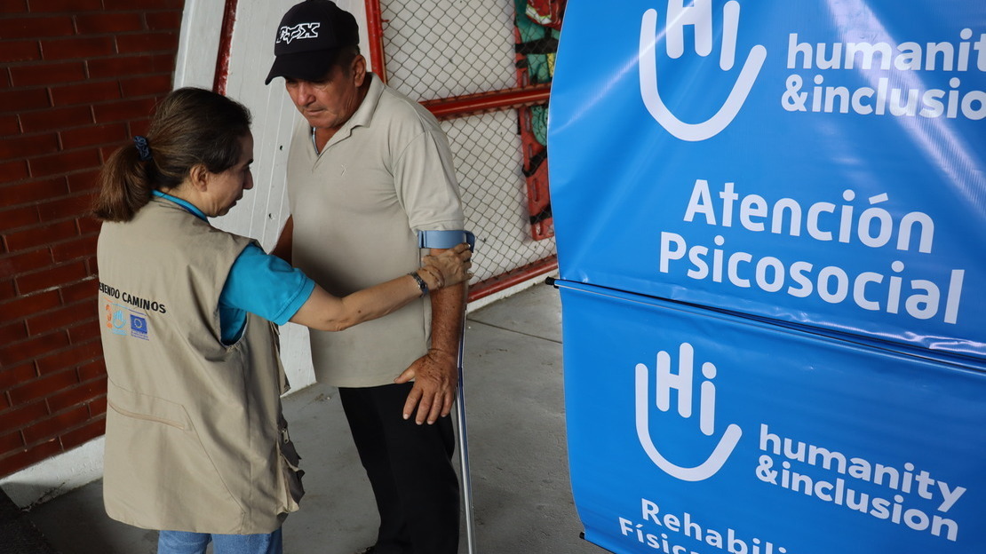 A woman helps a man hold a crutch.