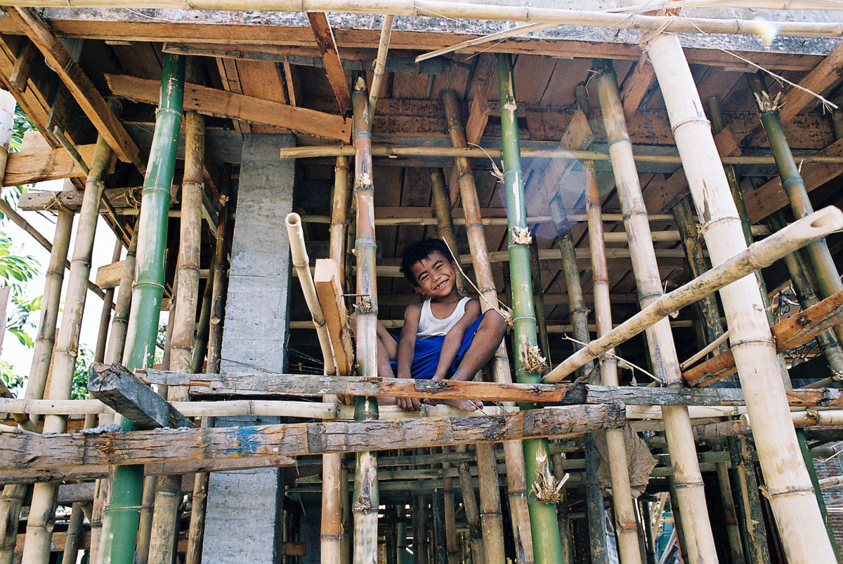 A little boy squats with a big smile in the middle of his bamboo dwelling.