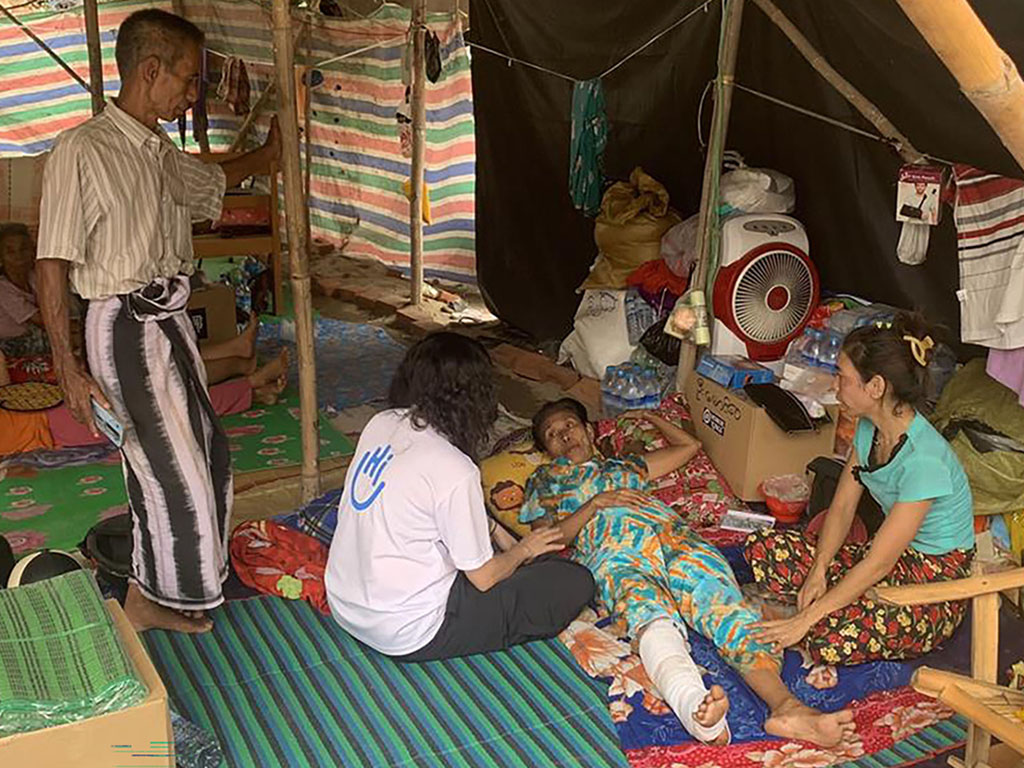 The woman lay down with her leg in a cast under a shelter speaking to people.