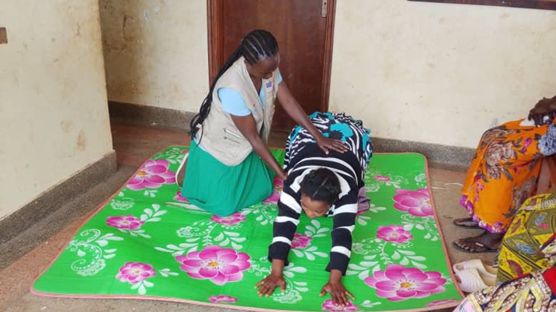 A woman is sitting on the floor, helping another to do an exercise.