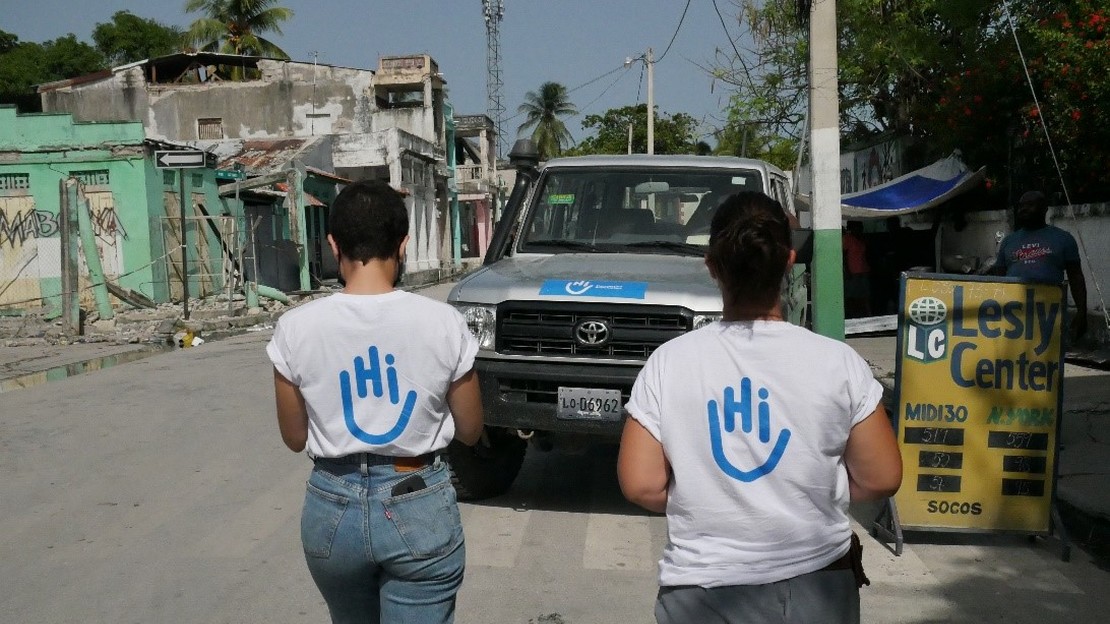 Two members of HI walk in a street in front of partly destroyed buildings