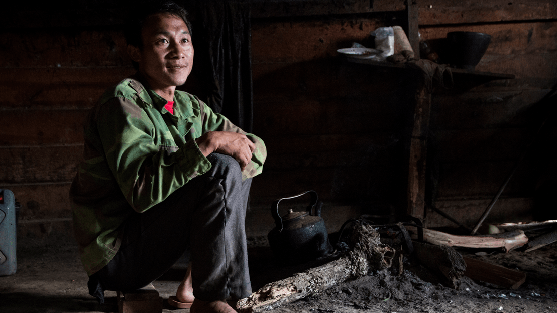 Man sitting on the ground in a dark room, smiling off into the distance