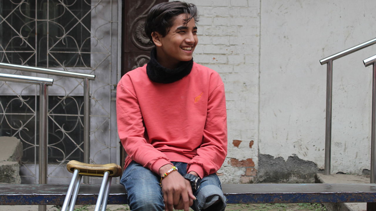 Young boy smiling wide and sitting next to crutches, in front of parallel bars