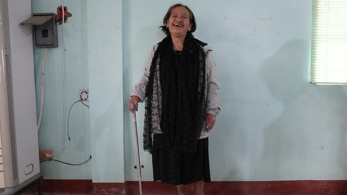 Nanay Benita is in the center of the photo, standing with her walking stick and smiling.